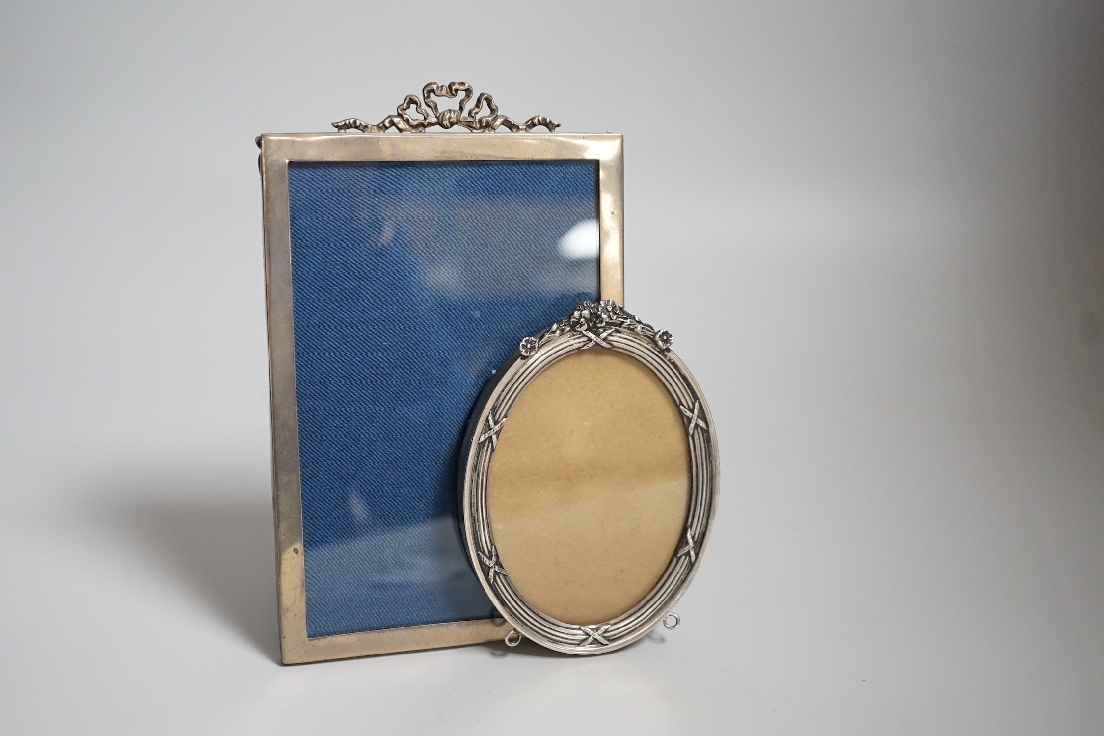 A George V silver mounted rectangular photograph frame, with ribbon bow crest, Birmingham, 1919, 16.1cm and an Edwardian silver mounted oval photograph frame by William Comyns, London, 1907.